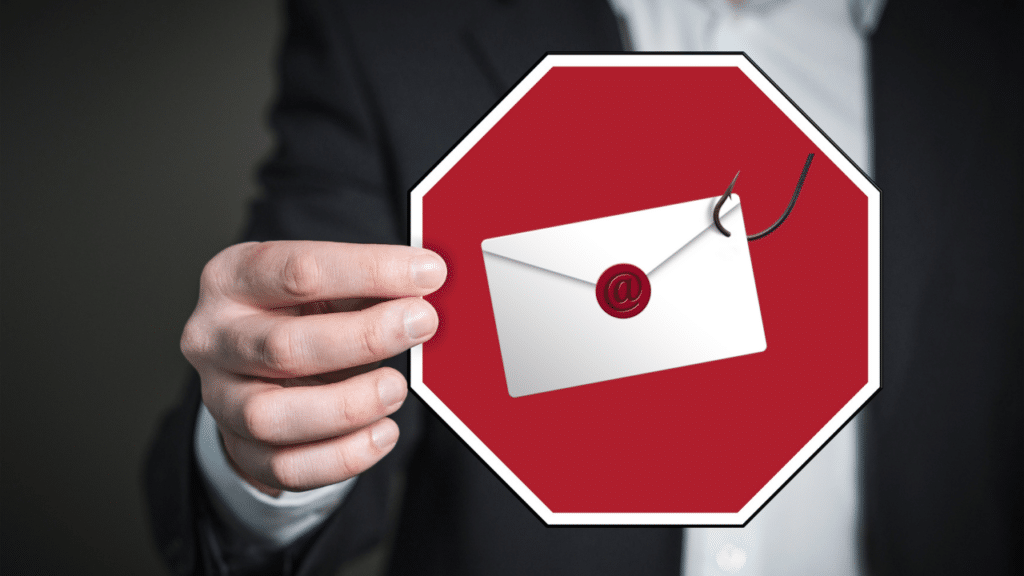 A man holds up a stop sign with an envelope snared with a fishing hook in the center.