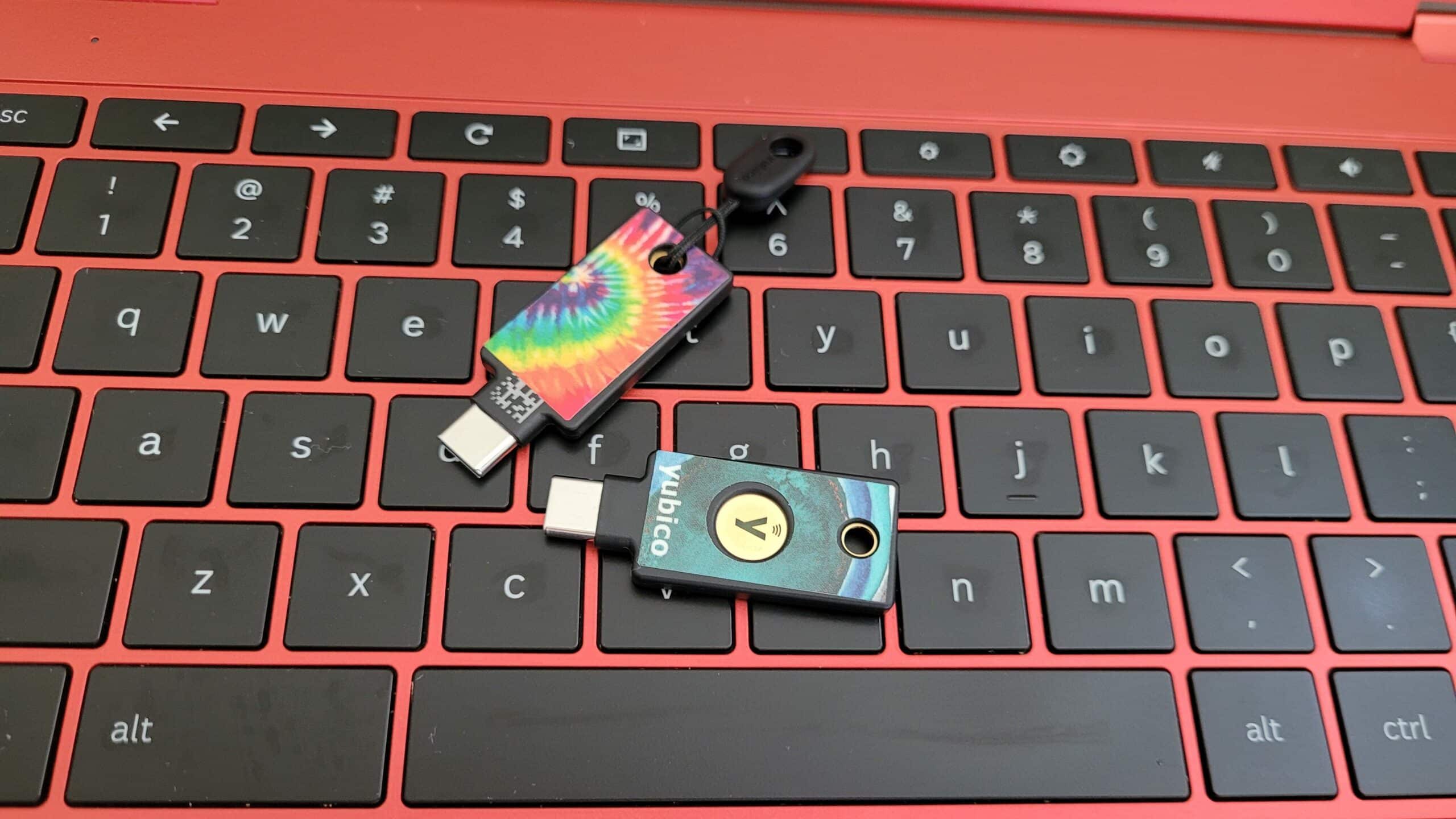 Two Yubikeys laying on the keyboard of a red Chromebook.