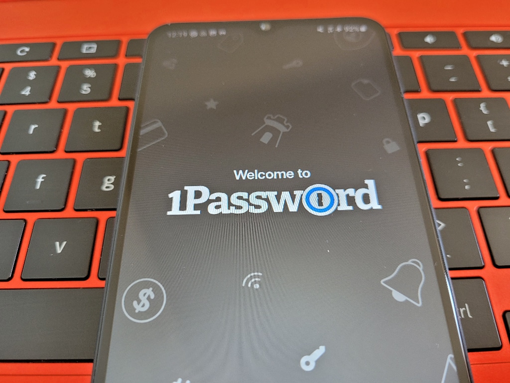 A phone with the 1Password app open sits on a red laptop.