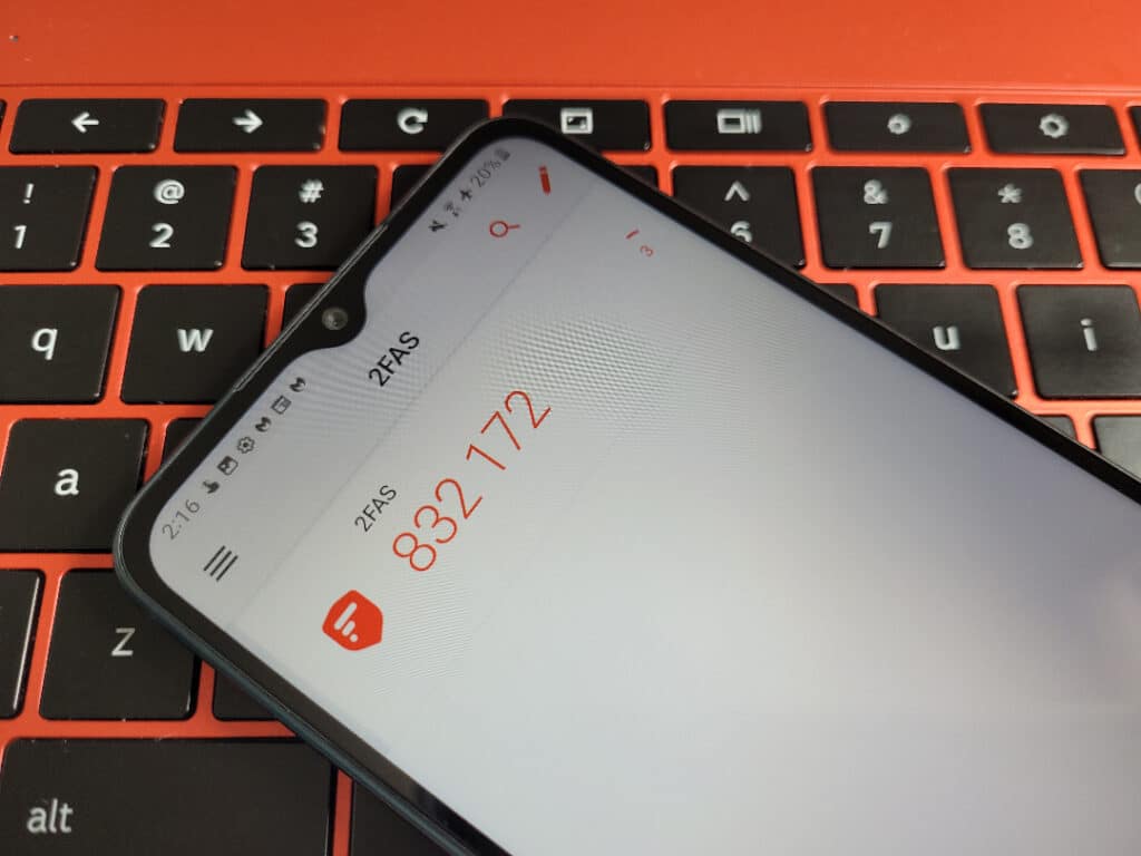 A phone on a laptop keyboard with the 2FAS authenticator app open. One code is displayed, which reads 832 172 and has 3 seconds remaining before it expires.