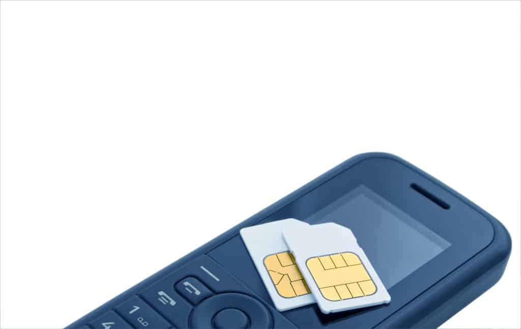 Two sim cards resting upon mobile telephone on white insulated background.