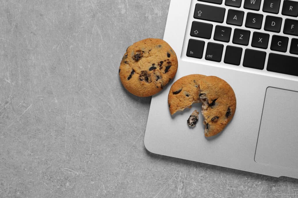Chocolate chip cookies and laptop on light grey table, flat lay.