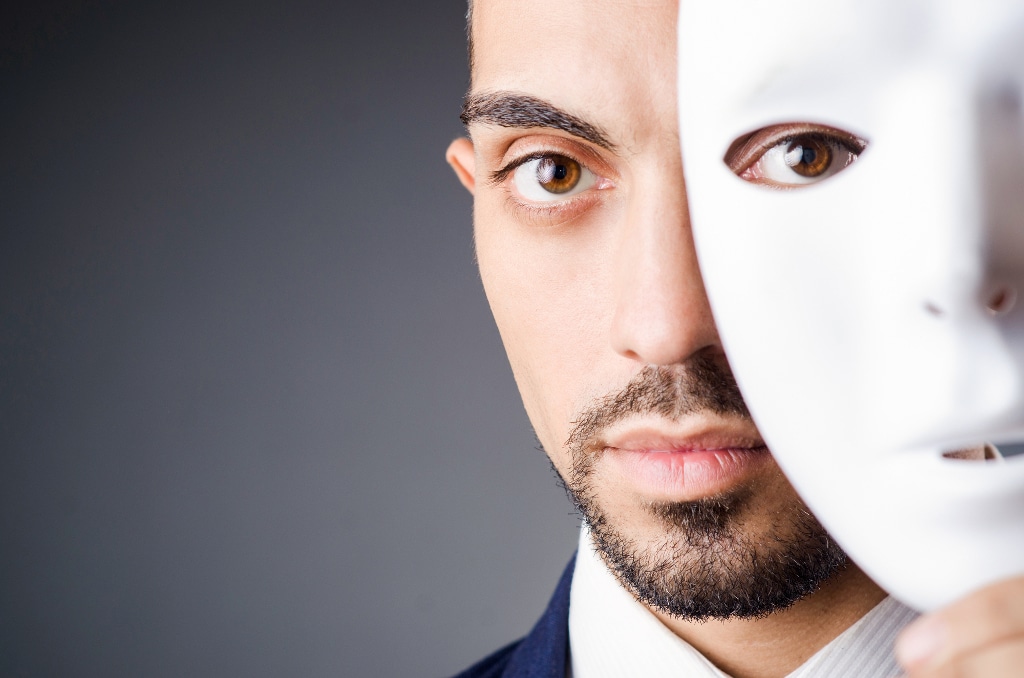 A close up of a man's face, which has a white mask covering half of it.