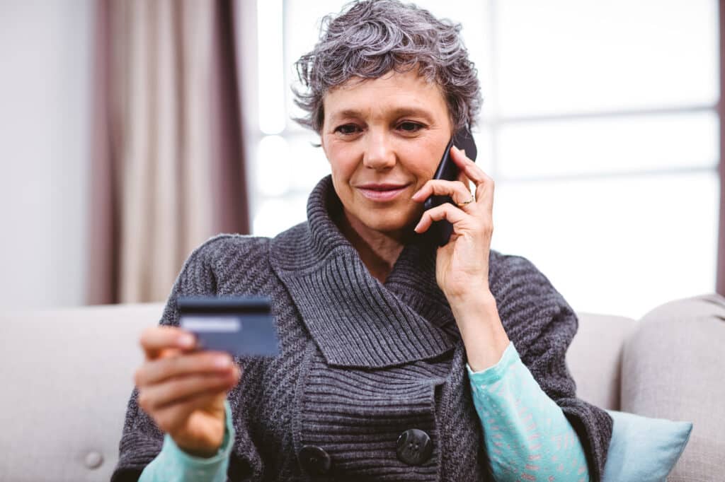 Close-up of mature woman holding credit card while talking on mobile phone at home
