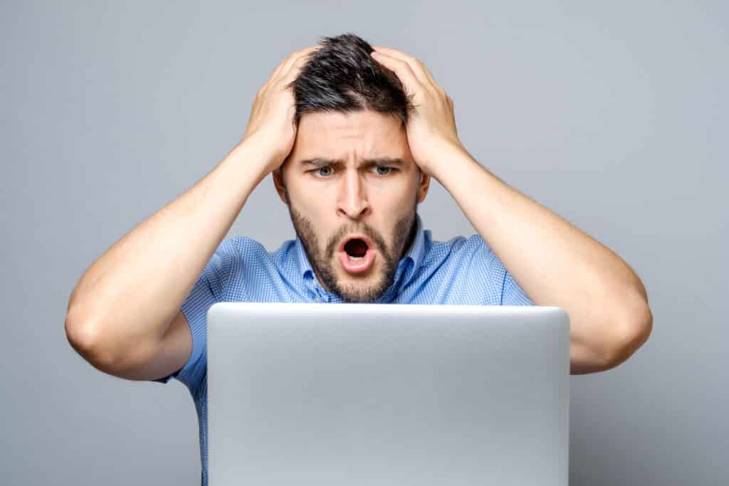 Young shocked man dressed in blue shirt while using laptop. Isolated on gray