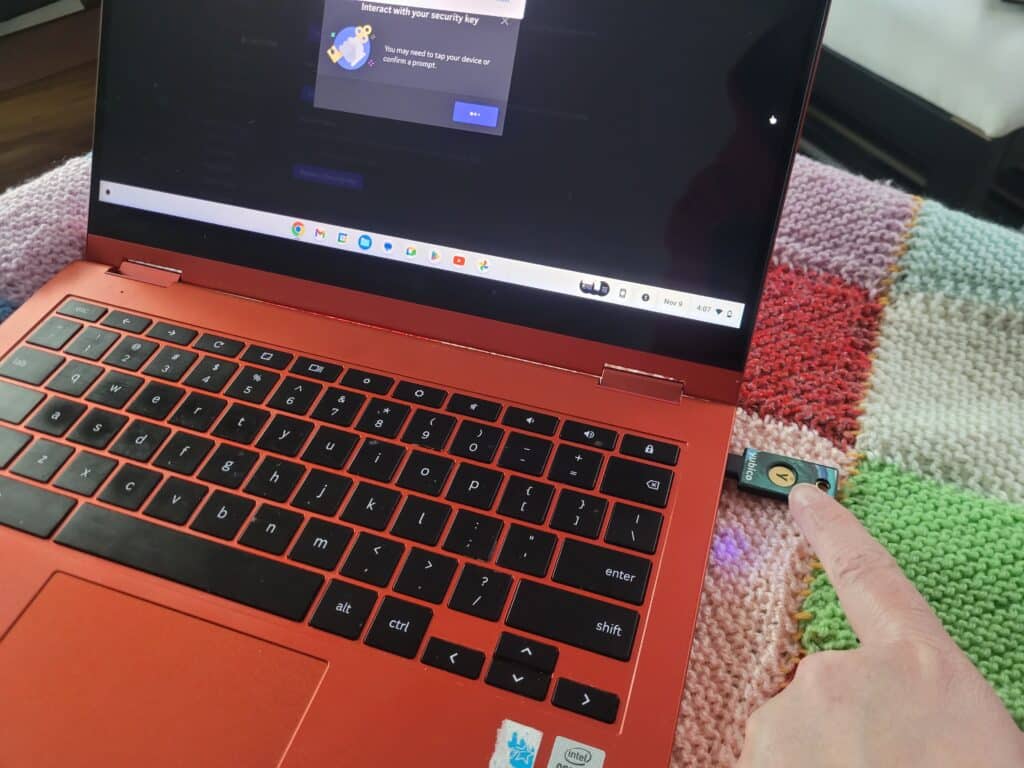 A finger tapping on a security key that is plugged into a red Chromebook.