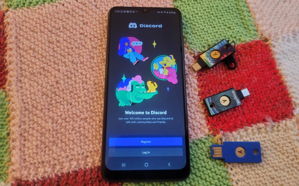 A phone with the Discord log in screen that reads "Welcome to Discord Join over 100 million people who use Discord to talk with communities and friends. Register. Login" Next to the phone are three security keys.