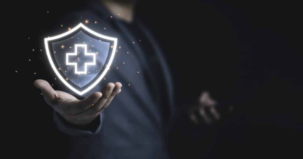 A man holding a shield with a healthcare cross inside of it.